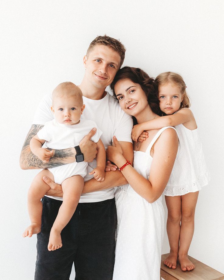 a man, woman and two children are posing for a family photo in front of a white wall