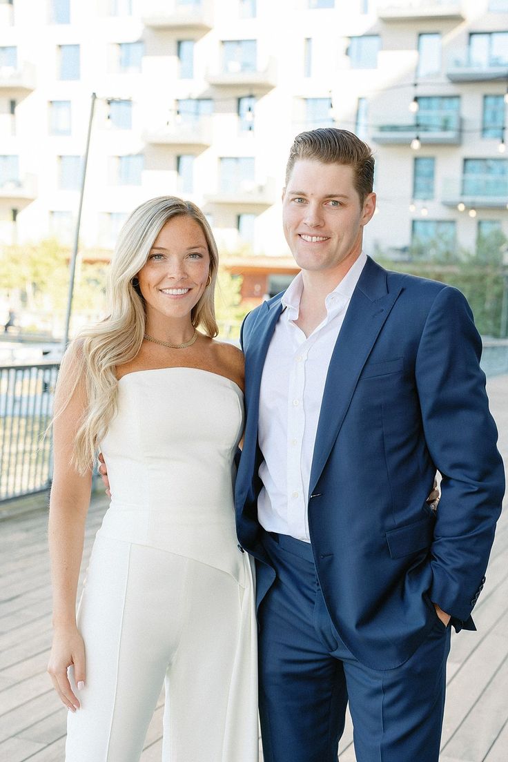 a man and woman standing next to each other in front of a building with tall windows