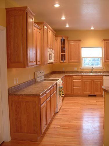 an empty kitchen with wooden cabinets and white appliances in the center, and a large window over the sink