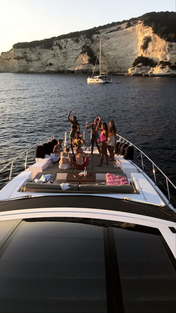 group of people sitting on the back of a boat in the water with cliffs behind them