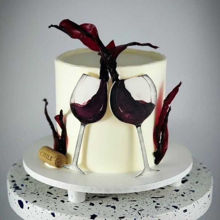 a white cake with two wine glasses on top and red leaves sticking out of it