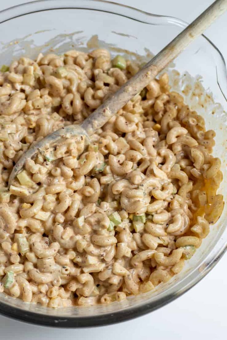 a bowl filled with macaroni and cheese on top of a table next to a wooden spoon