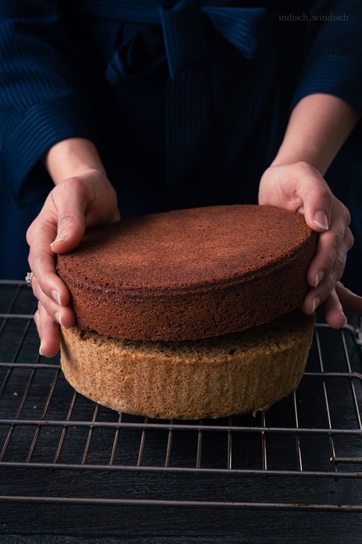 a person holding a cake on top of a cooling rack