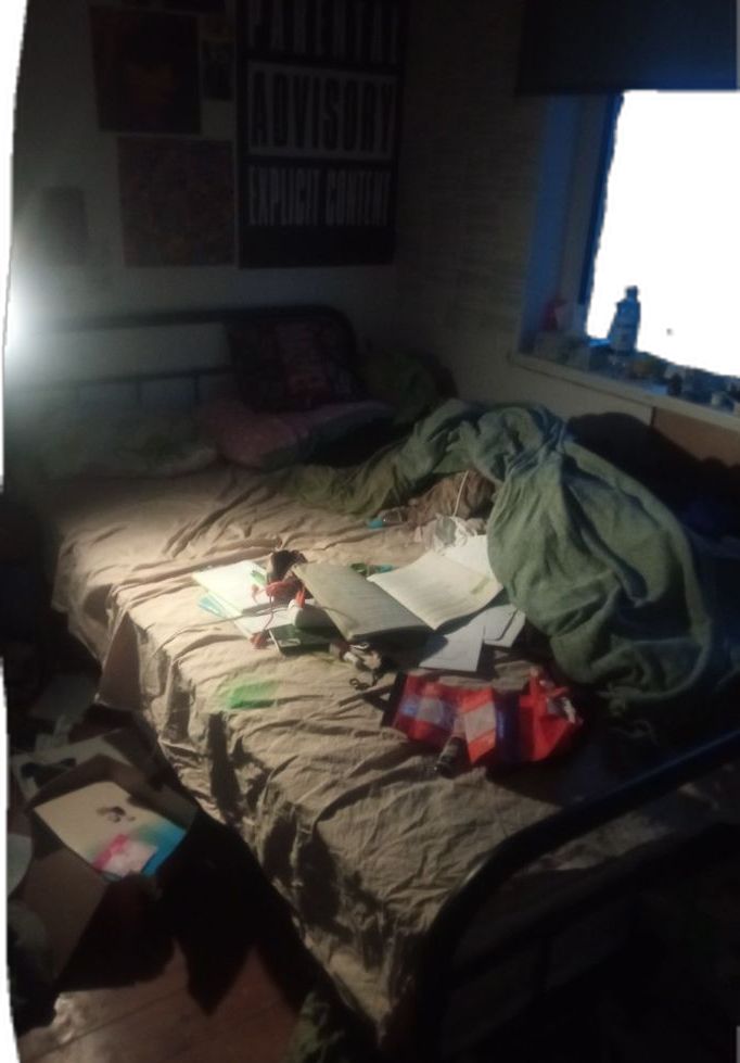 an unmade bed sitting next to a window in a room with lots of clutter