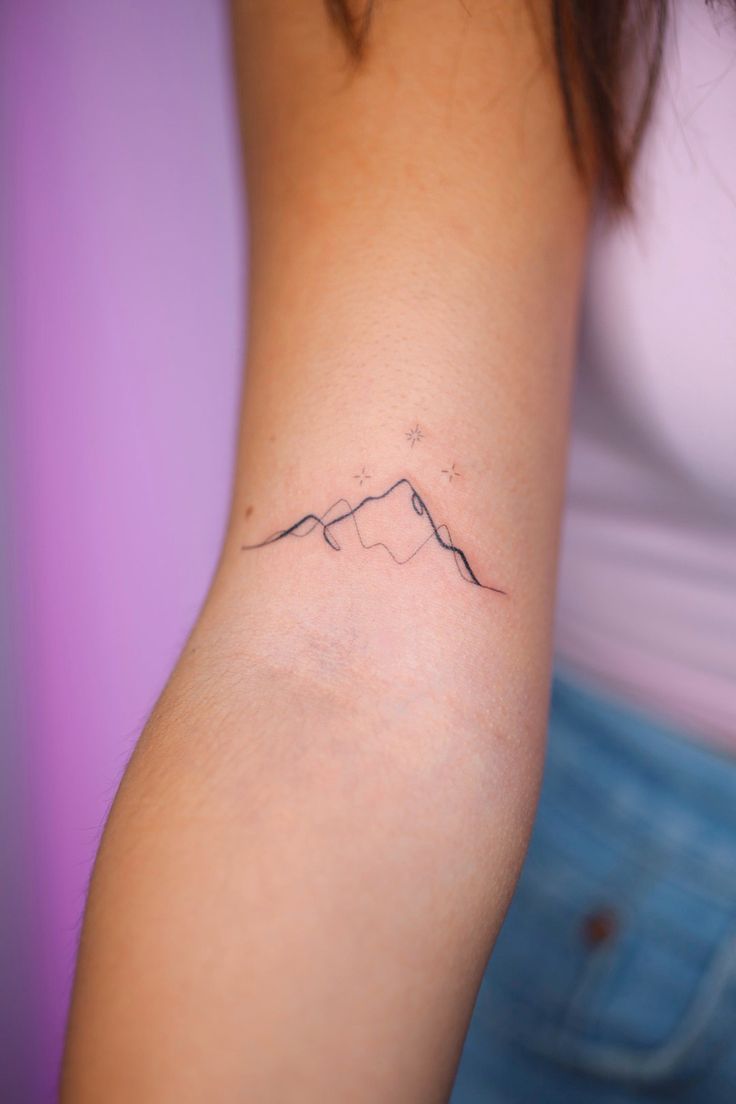 a woman's arm with a small mountain tattoo on the left side of her arm