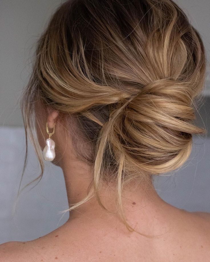 a woman with her hair in a low bun is seen from the back, wearing earrings