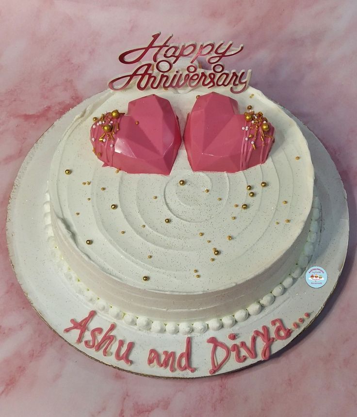 a white cake with two pink hearts on top and happy anniversary written on the side