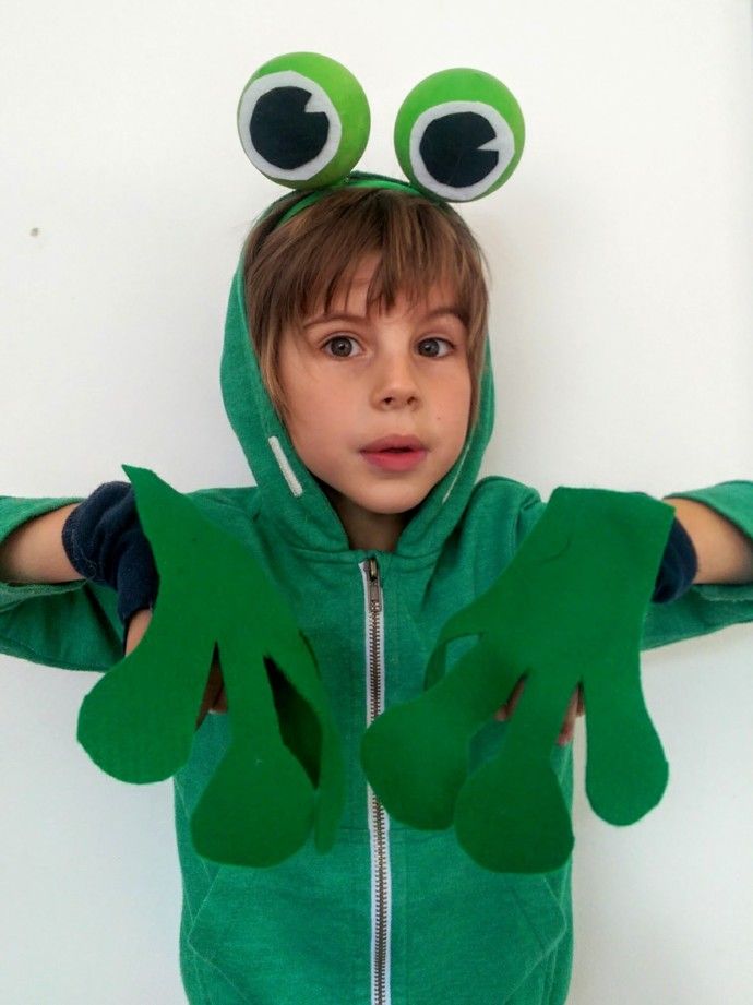 a young boy wearing a frog costume with his hands in the air and two googly eyes on his face