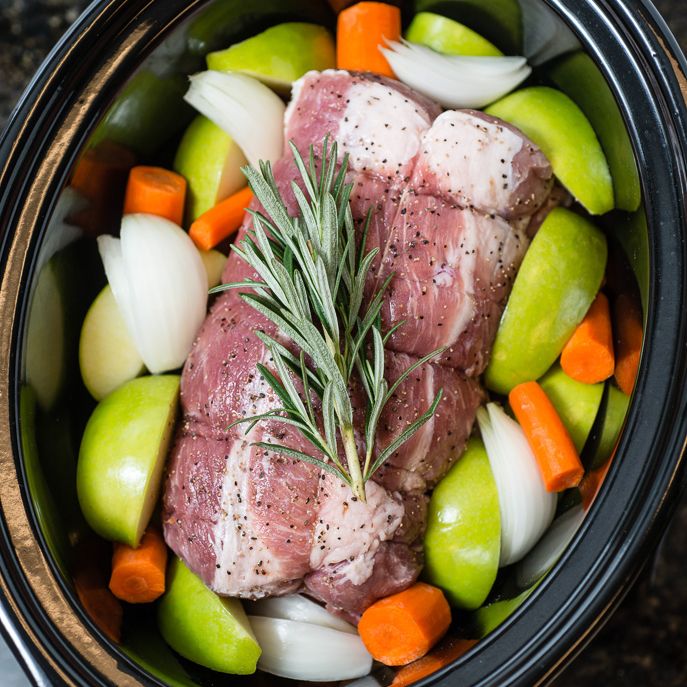 meat and vegetables in a slow cooker with seasoning sprig on top