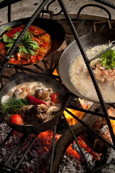 three pans filled with food cooking over an open fire