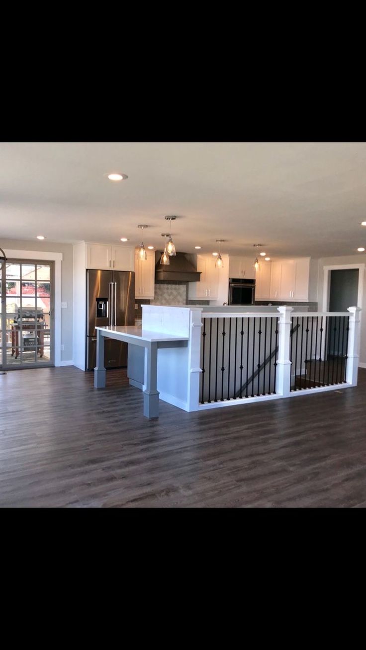 an empty living room with hard wood flooring and white cabinets in the kitchen area