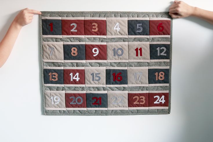 two hands are holding up a quilted wall hanging with numbers and times on it