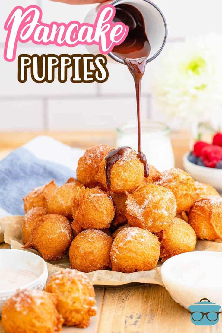 a person pouring syrup over some food on top of a wooden table with strawberries