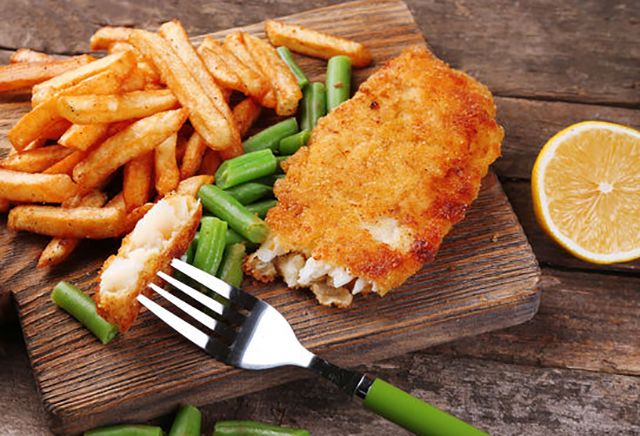 fish and french fries on a wooden cutting board with a lemon wedge next to it