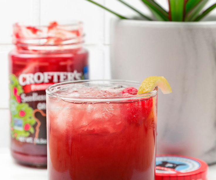 a glass filled with red liquid next to two cans of cranberry lemonade