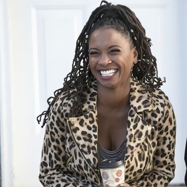 a smiling woman holding a coffee cup and wearing a leopard print jacket with braids on her hair