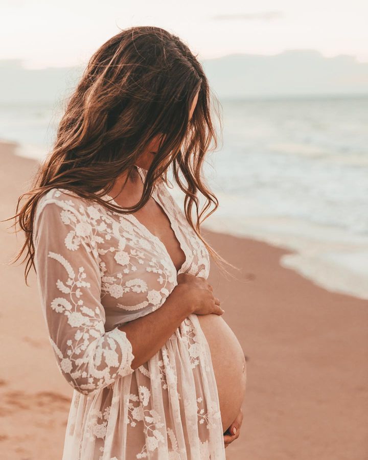 a pregnant woman standing on the beach with her belly in her hands and looking at the ocean