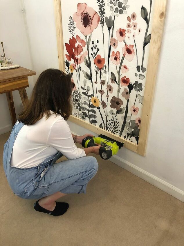 a woman kneeling down in front of a painting with flowers on the wall behind her