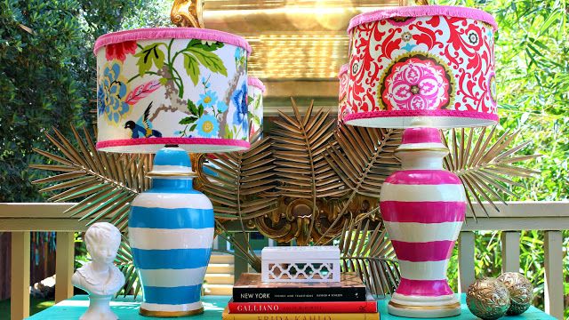 three colorful lamps sitting on top of a table next to books and vases in front of a mirror