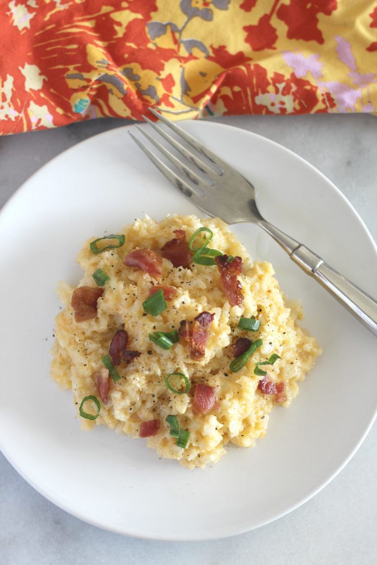 a white plate topped with mashed potatoes covered in bacon and green onions next to a fork