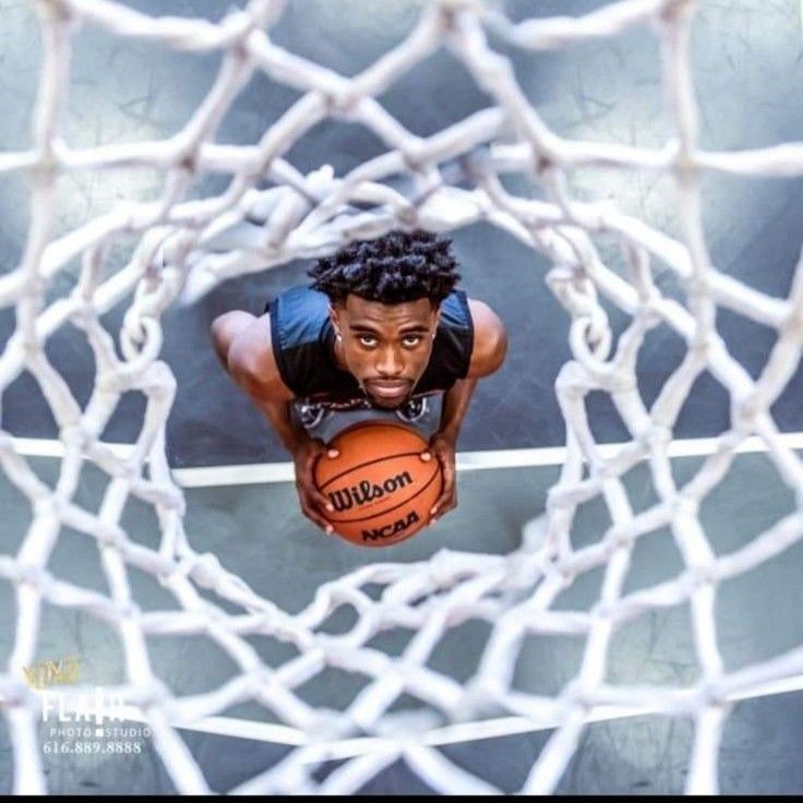 a young man holding a basketball in front of a net with his hands on the rim