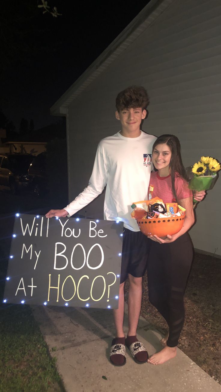 a young man and woman holding a sign that says will you be my boo at hoco?