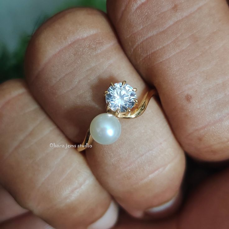 a close up of a person holding a ring with a pearl on the middle finger