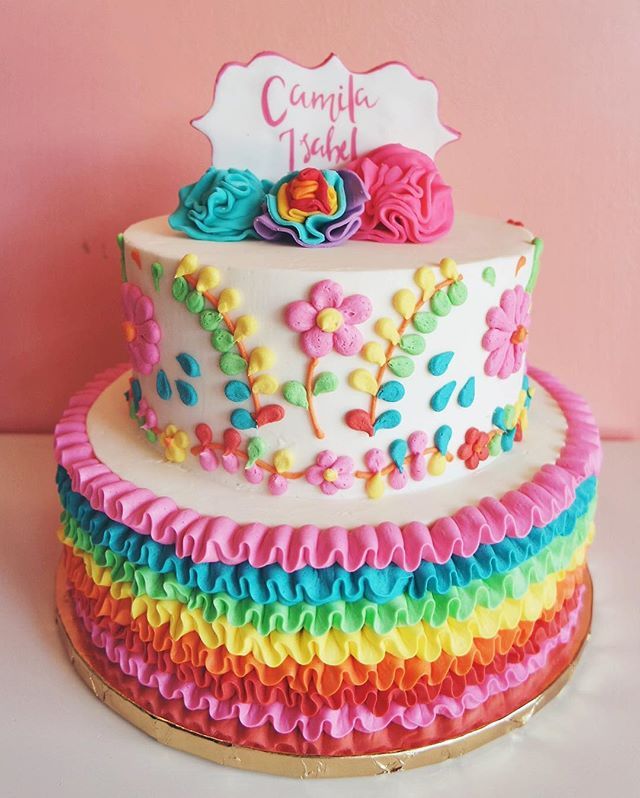 a cake that is decorated with rainbow ruffles and has a name on it