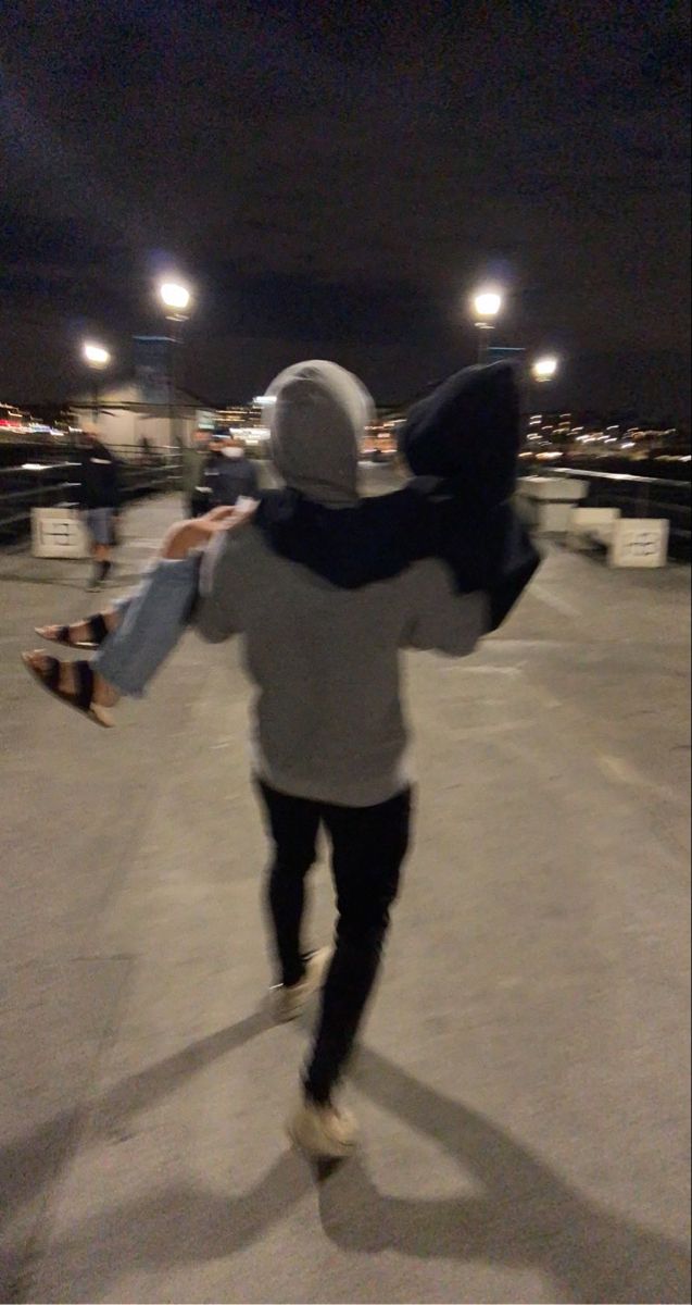 a young man riding a skateboard across a parking lot at night with other people in the background