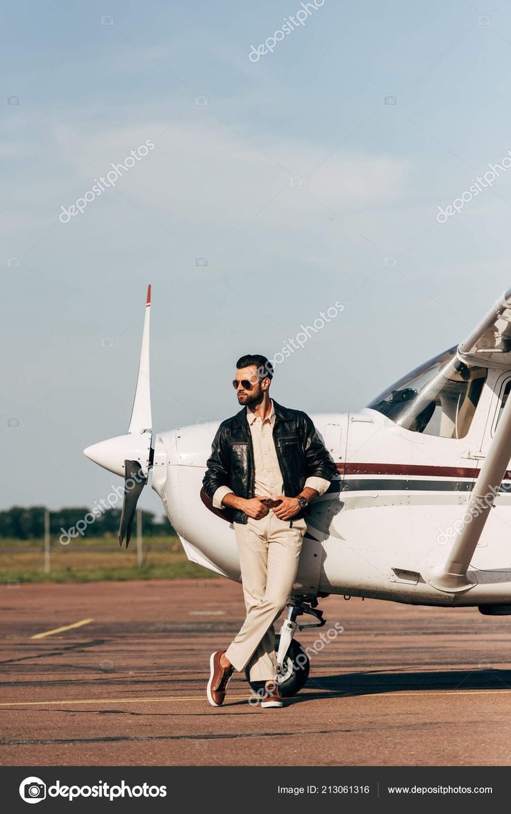 a man standing in front of an airplane on the tarmac with his legs crossed