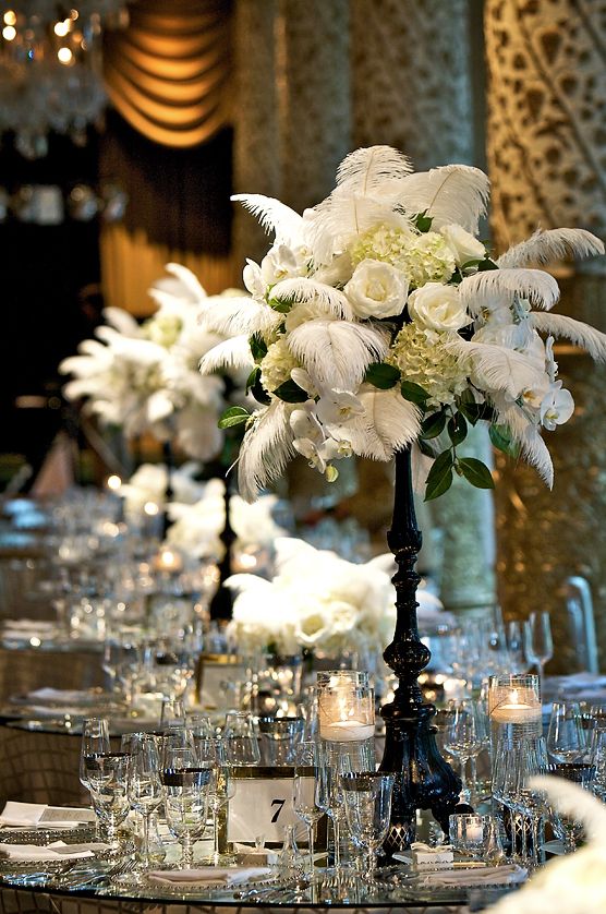 a tall vase filled with white flowers on top of a long table covered in silverware