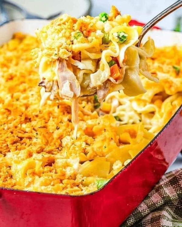 a spoon full of macaroni and cheese being lifted from a red casserole dish