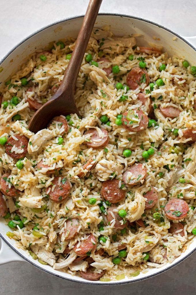 a large pot filled with rice and peas next to a wooden spoon on top of a table