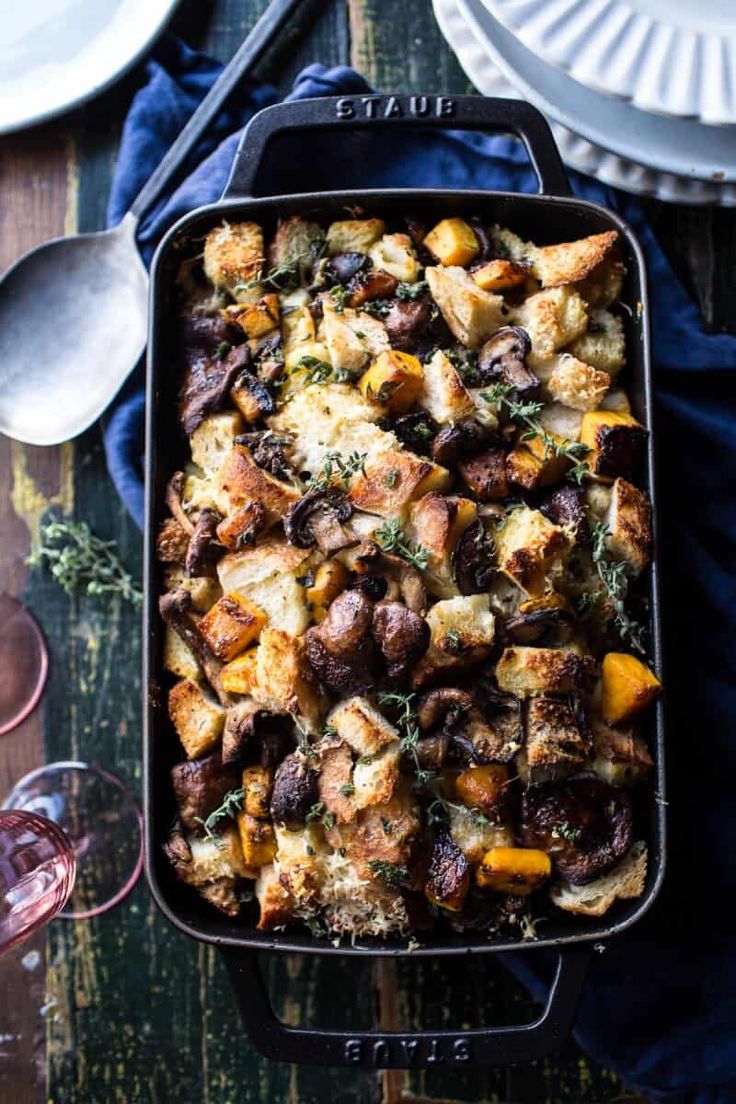 a casserole dish with meat and vegetables in it on a table next to wine glasses