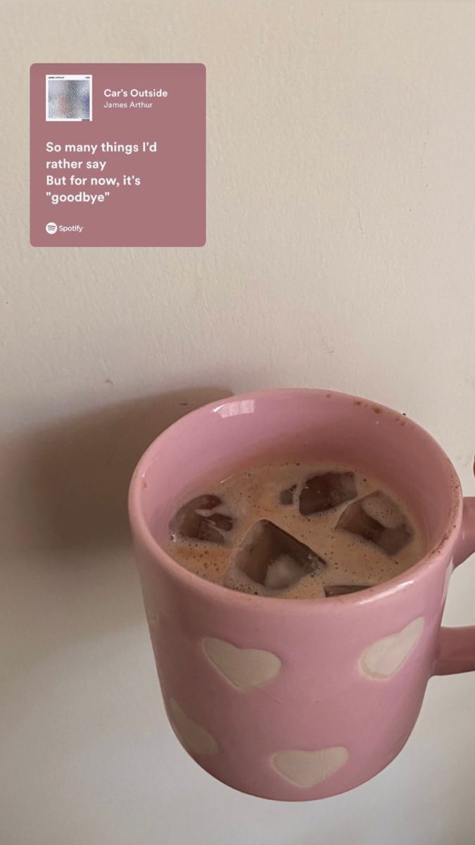 a pink coffee cup with ice cubes in it sitting on a table next to a white wall