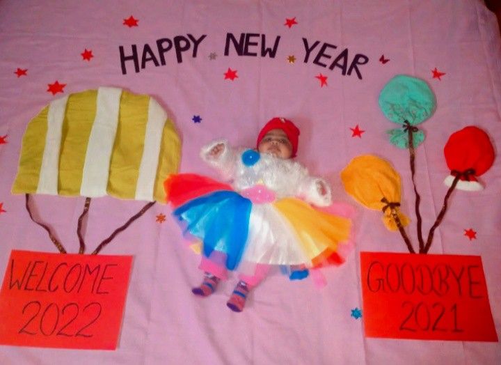 a baby laying on top of a pink blanket next to two balloons and some signs