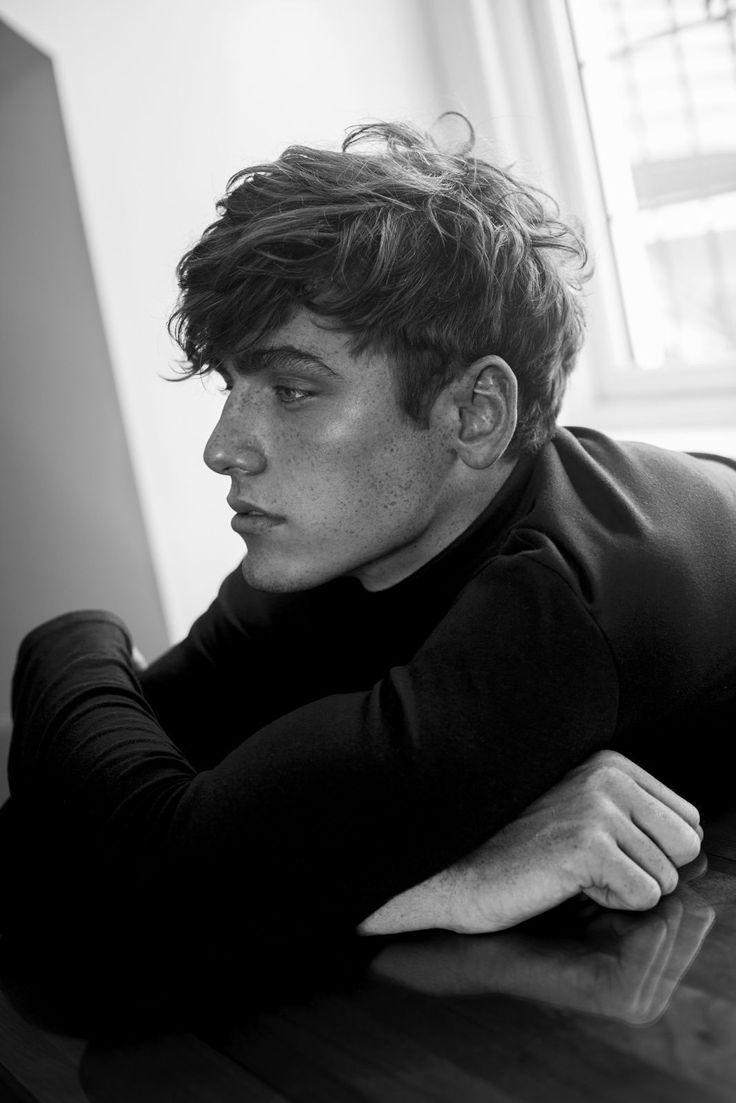 a young man laying on top of a wooden table next to a white wall and window