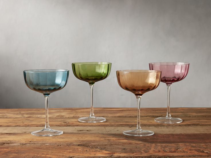 three different colored wine glasses sitting on top of a wooden table next to each other