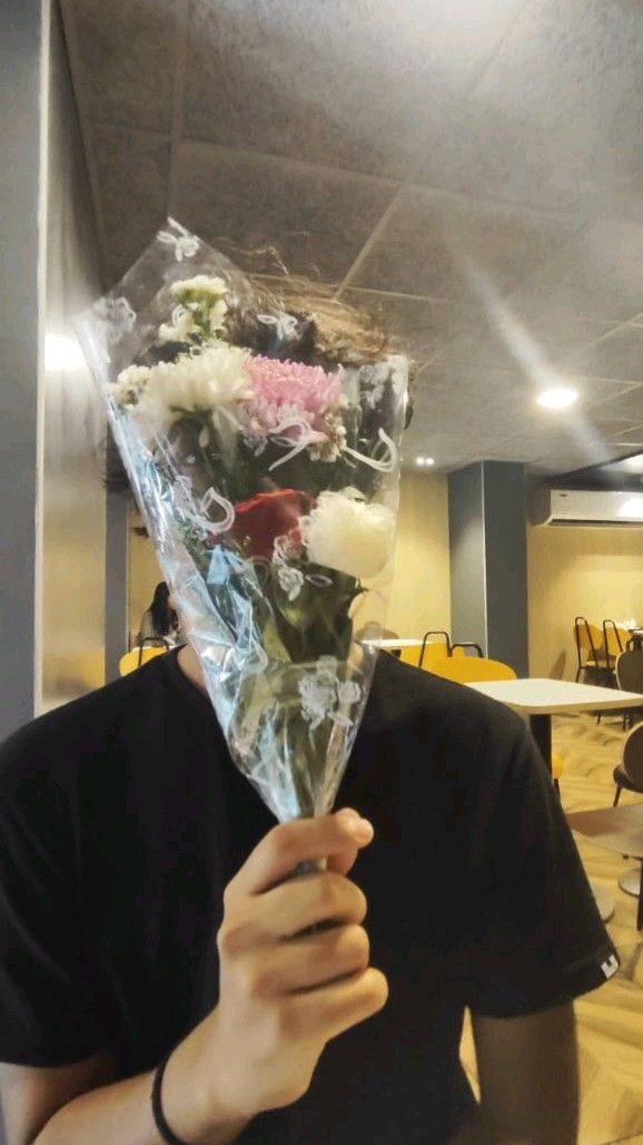 a man holding up a bouquet of flowers in front of his face and looking at the camera