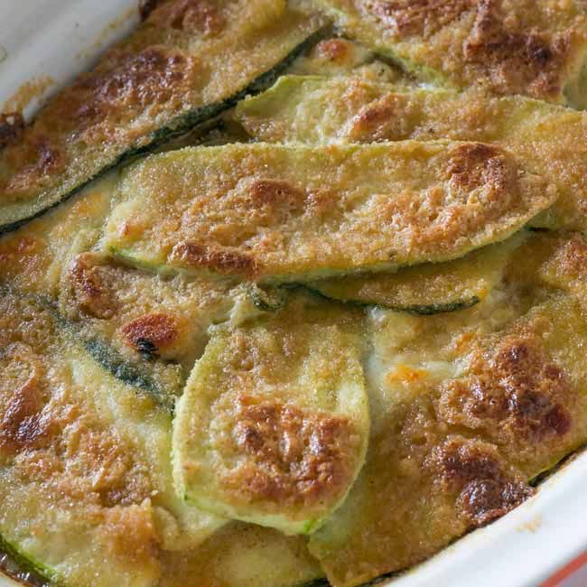 a casserole dish with zucchini and cheese on top, ready to be eaten