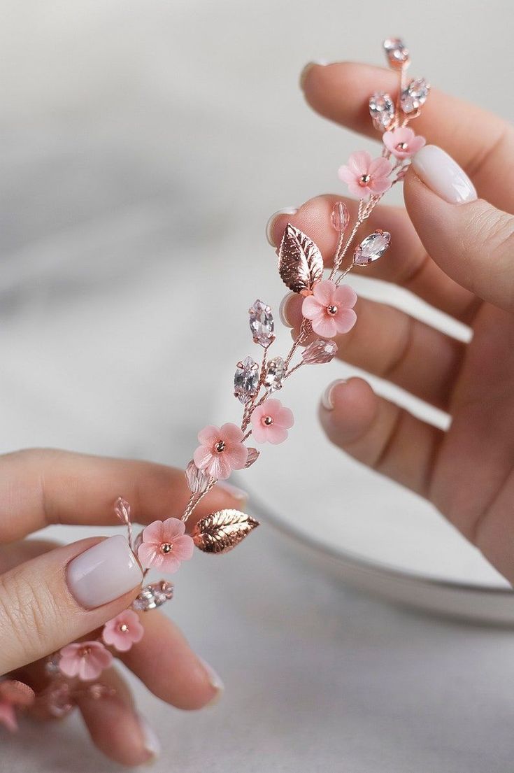 two hands with manicured nails and pink nail polish holding a flower shaped hair piece