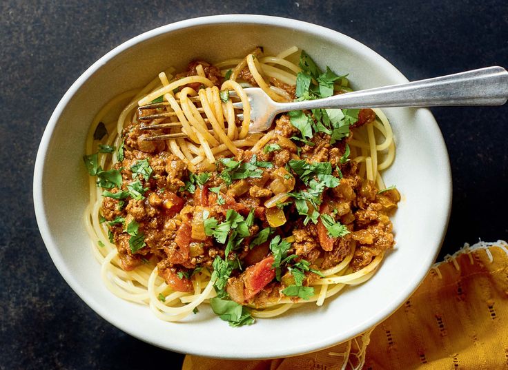 a white bowl filled with spaghetti and meat on top of a black table next to a slice of bread