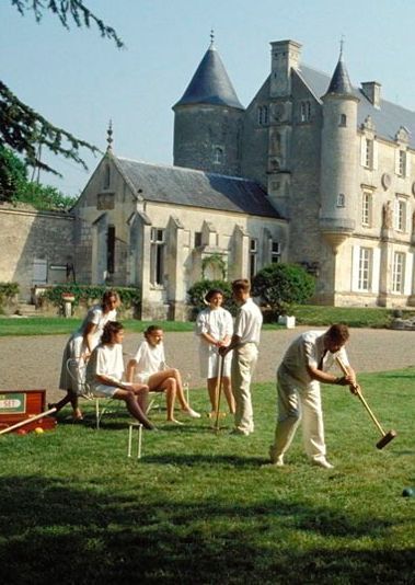 a group of people are playing croquet in front of a castle like building