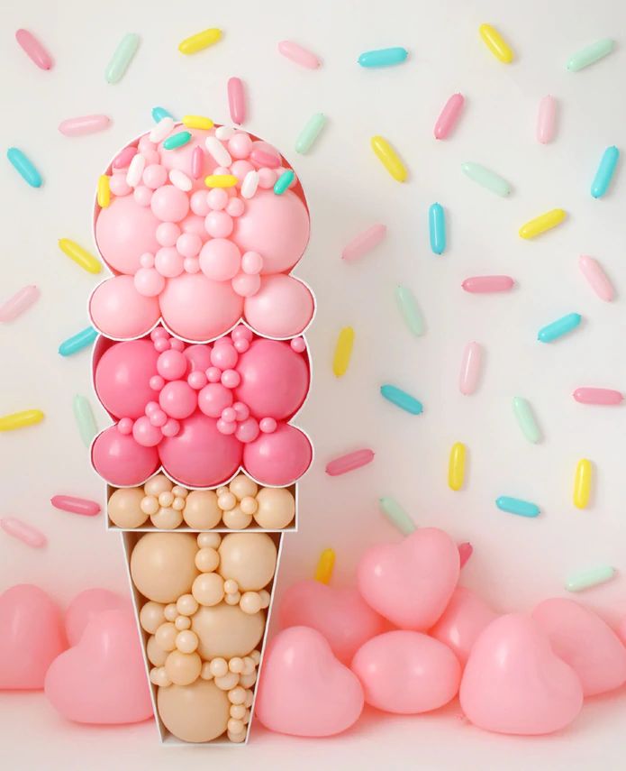 an ice cream cone filled with lots of pink and yellow sprinkles next to balloons