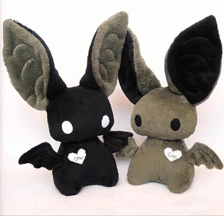 two small stuffed animals sitting next to each other on a white surface with one black and the other green