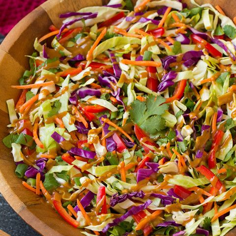 a wooden bowl filled with shredded carrots, cabbage and lettuce salad dressing