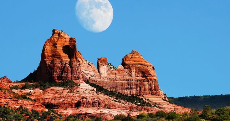 the full moon is setting over red rock formations