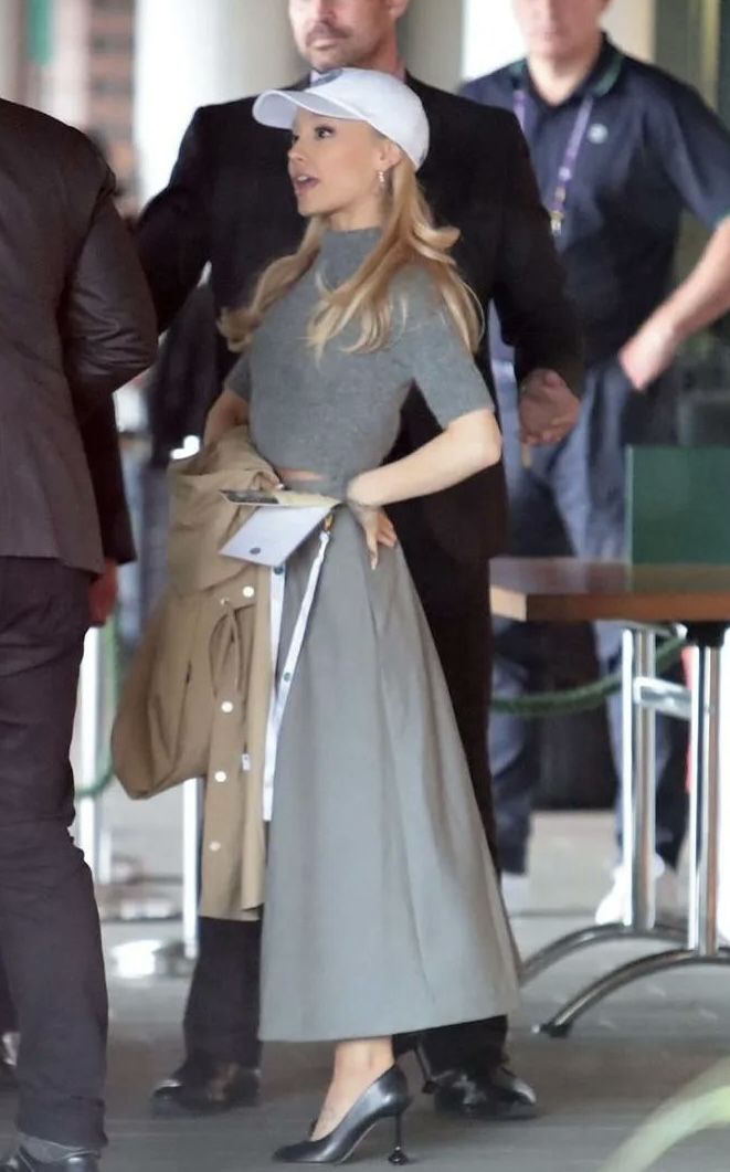 a woman in a gray dress and hat is walking through an airport with other people