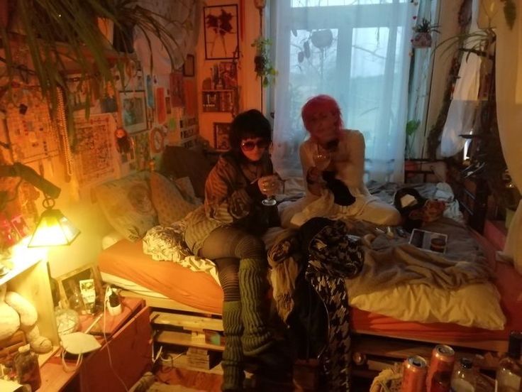 two women sitting on top of a bed in a room with lots of clutter