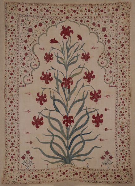 an embroidered wall hanging with red flowers and leaves on white ground, surrounded by ornate border